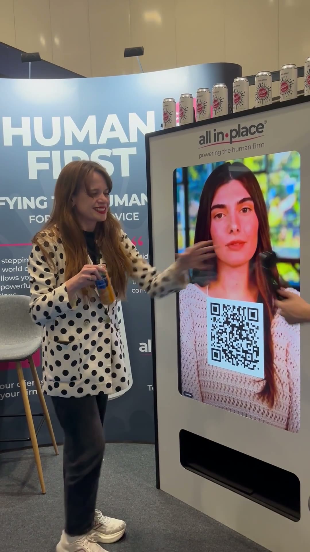 A guest holds the can the machine just released, the AI character still on screen behind her.