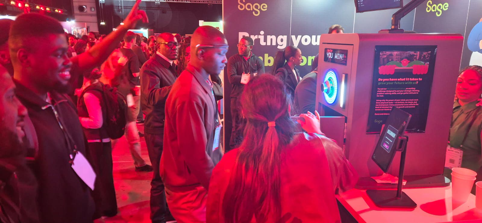 Guests queue and watch a player wearing the EEG headband at the Sage stand.